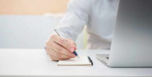 An employee uses pen, paper and a computer for Technology Planning.